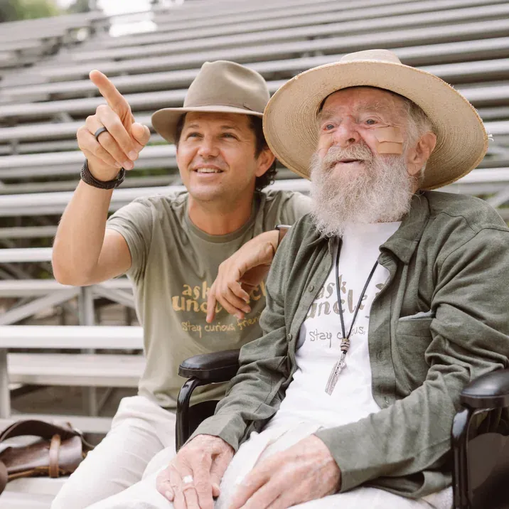 Uncle Jack, in a wide-brimmed hat, smiles beside a younger man in a hat who points into the distance.