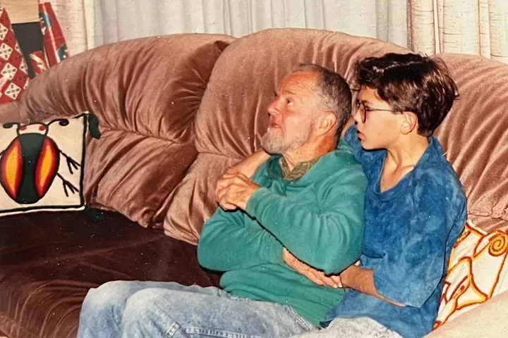 Two people sit close together on a brown velvet couch, arms folded.